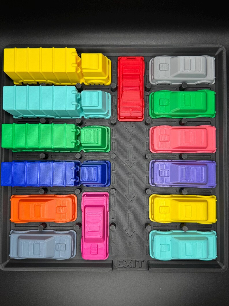 May include: A selection of brightly coloured toy trucks and cars arranged in a black tray. The vehicles are in various colours, including yellow, blue, red, green, and pink. The word "EXIT" is printed on the tray.