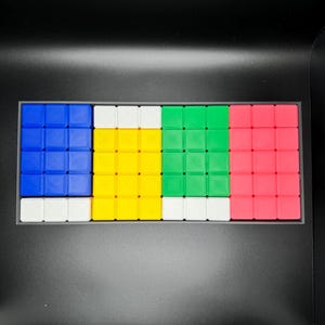 May include: A set of four 3x3 Rubik's Cube puzzles in a black case. The cubes are arranged in a row, with the colors blue, yellow, green, and pink.