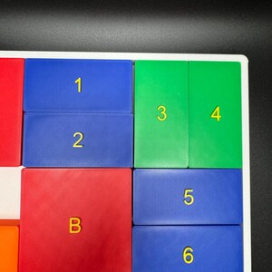 May include: A colorful set of square tiles with numbers 1 through 6 and the letter B. The tiles are arranged in a grid pattern. The tiles are made of a textured plastic material.