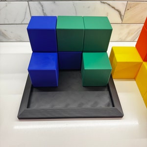 May include: A set of colorful wooden blocks stacked on a black tray. The blocks are blue, green, and yellow.