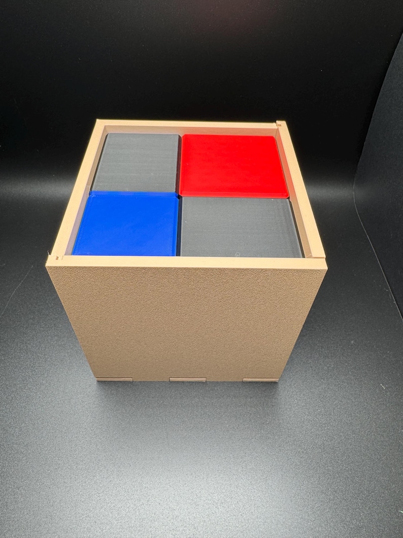 May include: A wooden box with four compartments, each containing a colored block. The blocks are red, blue, and two gray blocks.