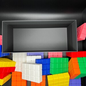 May include: A black box filled with colorful building blocks. The blocks are made of plastic and have a grid pattern. The blocks are in various colors, including red, orange, yellow, green, blue, purple, and white.