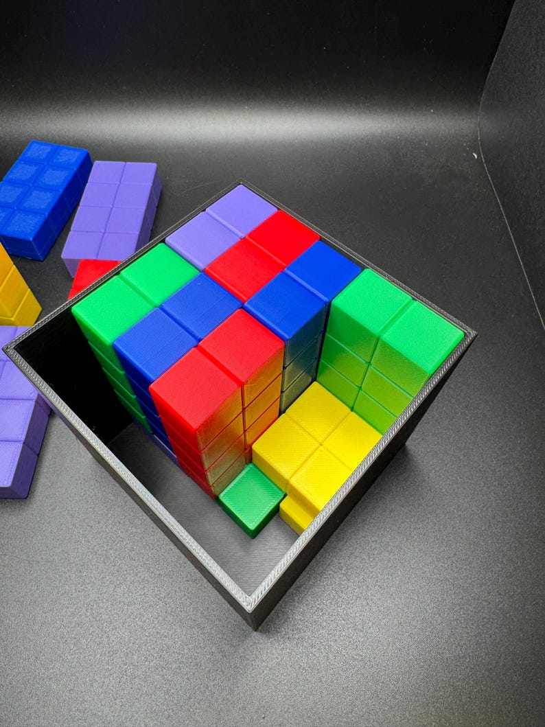May include: A colorful puzzle game featuring a cube-shaped frame filled with various colored blocks. The blocks are arranged in a grid pattern, with colors including red, green, blue, yellow, and purple. Additional blocks are visible outside the frame.