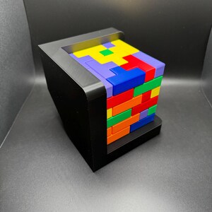 May include: A colorful block puzzle with a black base. The blocks are stacked in a tower and are arranged in a pattern. The blocks are red, orange, yellow, green, blue, and purple.