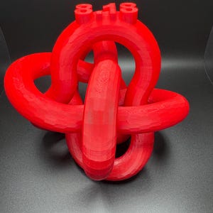 May include: A red 3D printed knot sculpture with the number "8-18" on top.