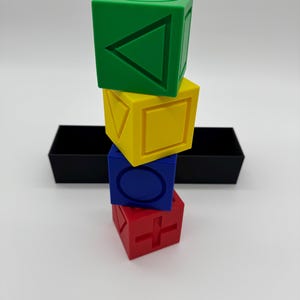 May include: A stack of four colorful blocks with different geometric shapes on each side. The blocks are green, yellow, blue, and red.