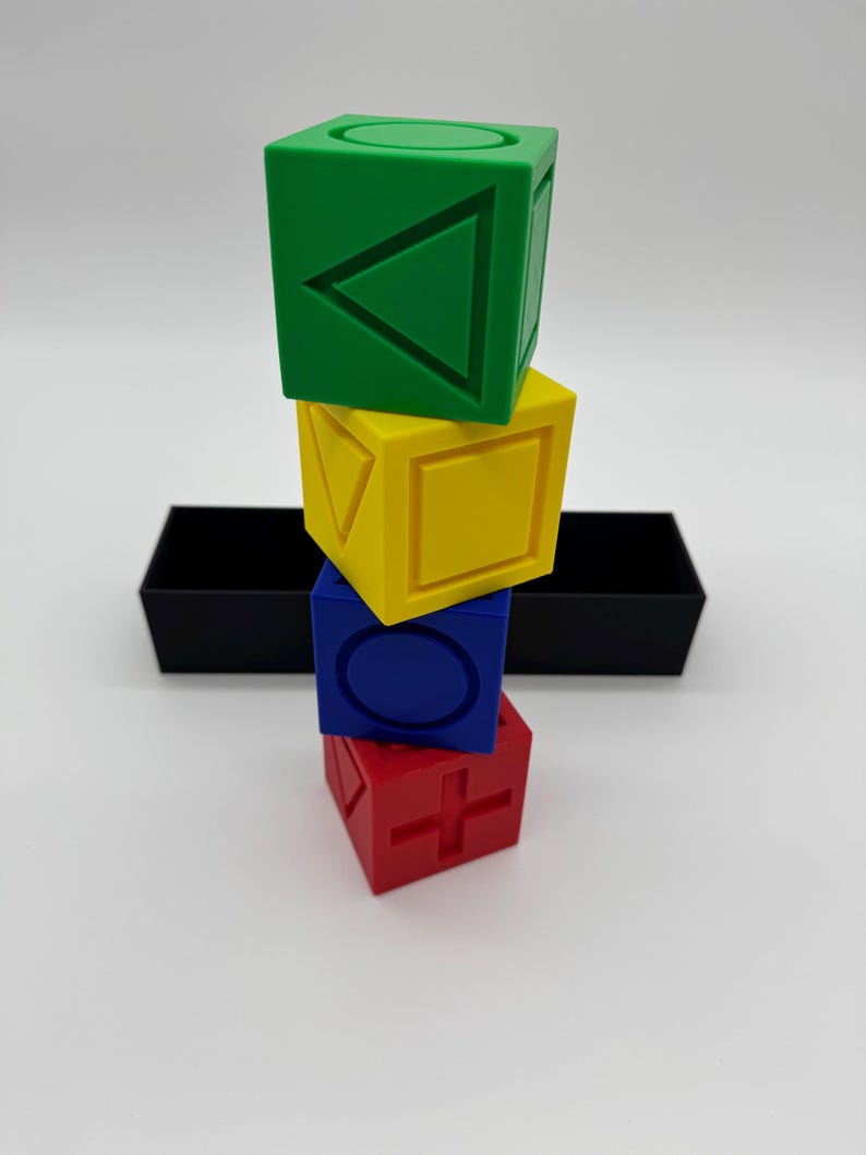 May include: A stack of four colorful blocks with different geometric shapes on each side. The blocks are green, yellow, blue, and red.