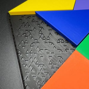Może przedstawiać: Geometriczna układanka z pięcioma elementami w r&oacute;żnych kolorach: ż&oacute;łtym, niebieskim, fioletowym, pomarańczowym i zielonym. Elementy są ułożone w kształt gwiazdy na czarnym tle.