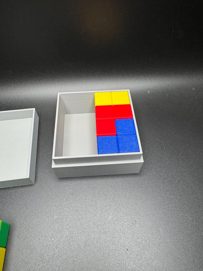 Puede incluir: Una caja gris con la tapa abierta, que revela un conjunto de bloques de madera de colores. Los bloques est&aacute;n dispuestos en un patr&oacute;n, con bloques amarillos, rojos y azules visibles. Los bloques est&aacute;n dispuestos en un patr&oacute;n, con bloques amarillos, rojos y azules visibles.