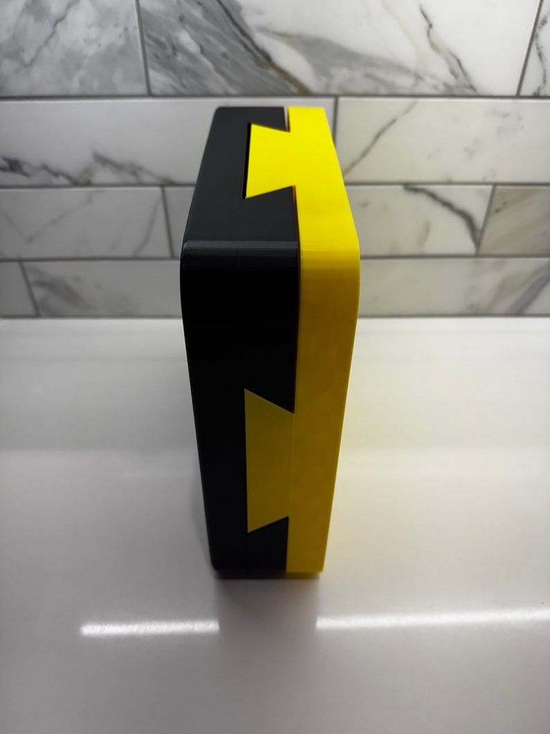 May include: A black and yellow box with a lightning bolt design. The box is made of a hard plastic material and has a smooth finish.