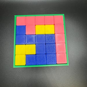 May include: A colorful puzzle game with a green frame. The game features a grid of small squares in pink, yellow, and blue. The pieces are arranged in a Tetris-like pattern, offering a fun and engaging challenge for puzzle enthusiasts.