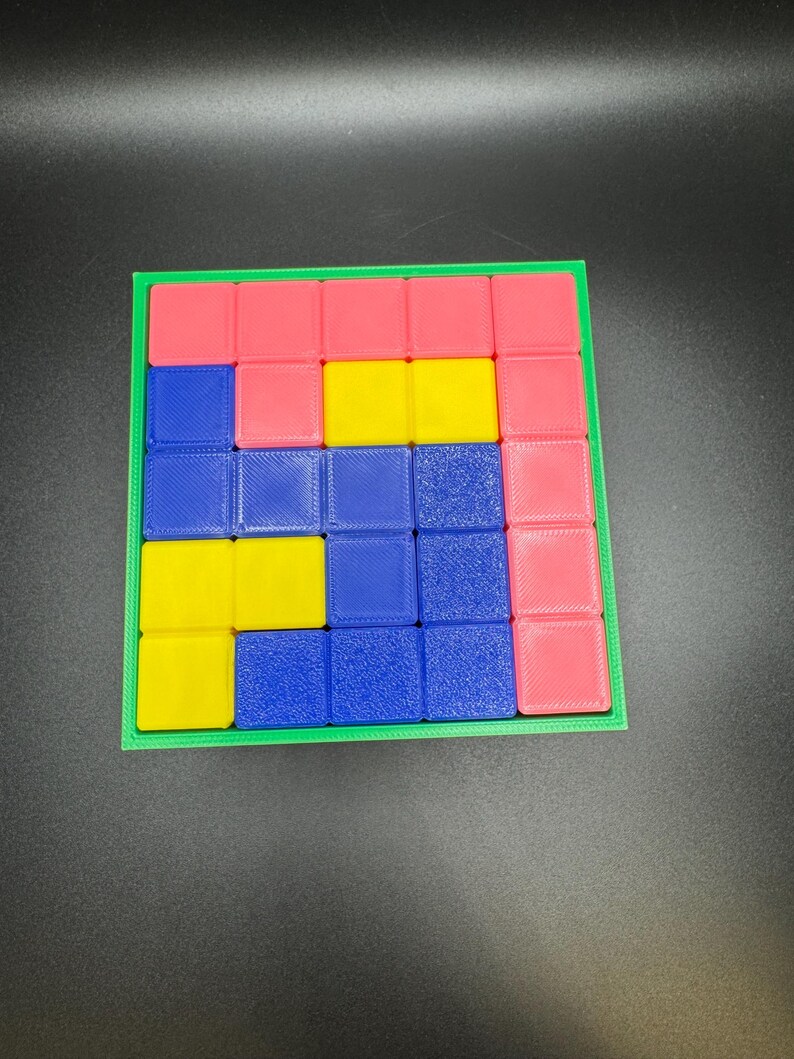 May include: A colorful puzzle game with a green frame. The game features a grid of small squares in pink, yellow, and blue. The pieces are arranged in a Tetris-like pattern, offering a fun and engaging challenge for puzzle enthusiasts.