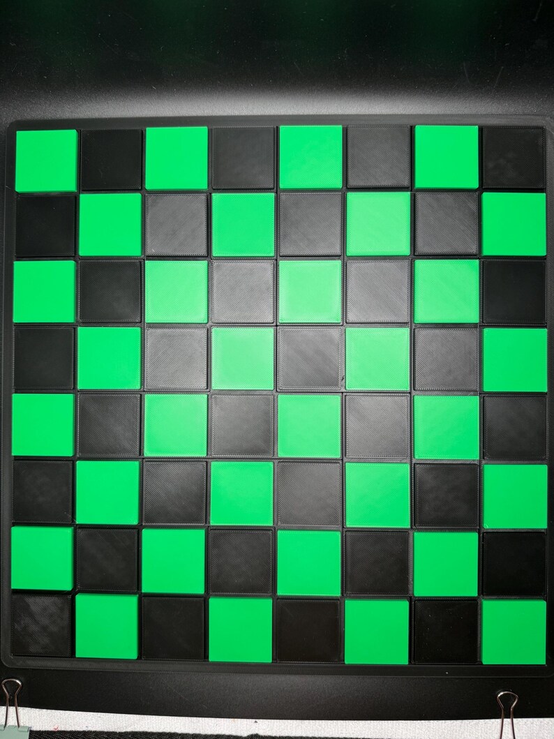 K&ouml;nnte beinhalten: Ein quadratisches Schachbrett mit schwarzem Rand. Das Brett weist ein Muster aus abwechselnd schwarzen, grauen und leuchtend gr&uuml;nen Quadraten auf. Die Quadrate sind gleich gro&szlig; und in einem Raster angeordnet, wodurch ein klassisches Schachbrettmuster entsteht.