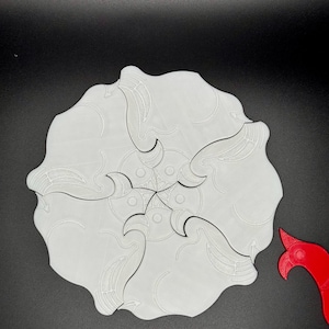 May include: A white, 3D printed, circular puzzle with five interlocking pieces. The pieces have a wave-like design and are arranged in a starburst pattern.