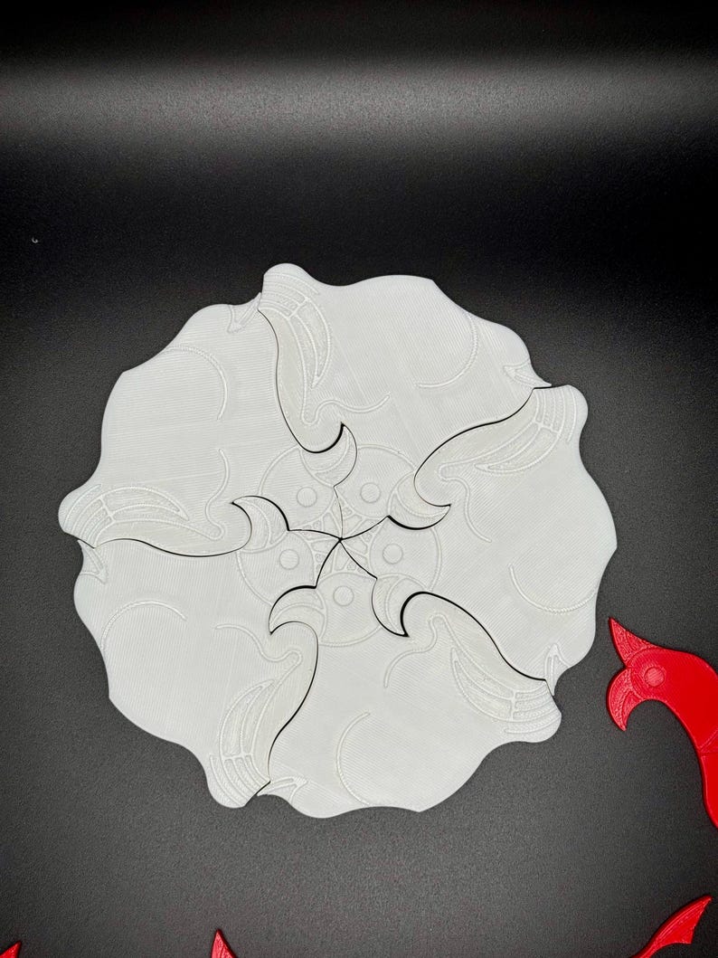 May include: A white, 3D printed, circular puzzle with five interlocking pieces. The pieces have a wave-like design and are arranged in a starburst pattern.