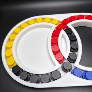 May include: A white plastic sorting tray with multiple circular compartments arranged in an interlocking pattern. The tray contains numerous small, round, flat-topped pegs in yellow, red, black, and blue colours, organised within the sections.