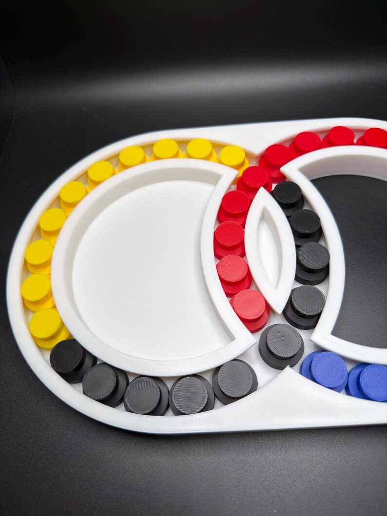 May include: A white plastic sorting tray with multiple circular compartments arranged in an interlocking pattern. The tray contains numerous small, round, flat-topped pegs in yellow, red, black, and blue colours, organised within the sections.