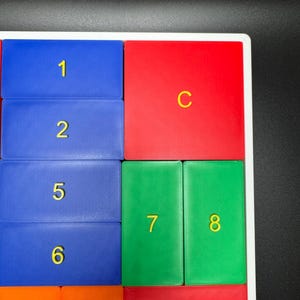 K&ouml;nnte beinhalten: Ein wei&szlig;er Rahmen mit bunten Fliesen. Die Fliesen sind mit den Zahlen 1, 2, 5, 6, 7, 8, 9, 10 nummeriert. Die Fliesen sind auch mit den Buchstaben C und B beschriftet.