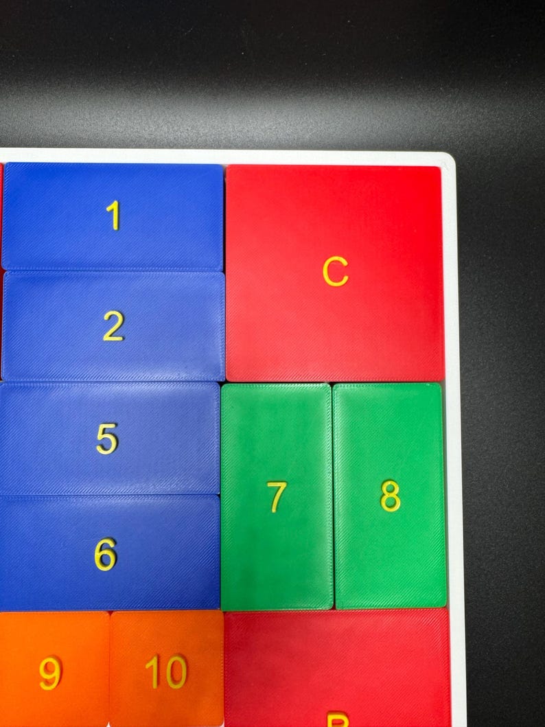 K&ouml;nnte beinhalten: Ein wei&szlig;er Rahmen mit bunten Fliesen. Die Fliesen sind mit den Zahlen 1, 2, 5, 6, 7, 8, 9, 10 nummeriert. Die Fliesen sind auch mit den Buchstaben C und B beschriftet.