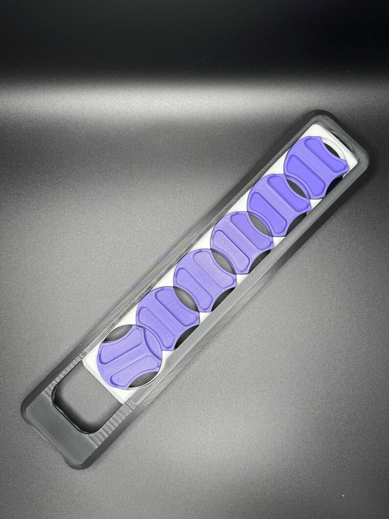 May include: A black plastic case with a handle holds eight purple guitar picks. The picks are arranged in a row and are visible through the clear plastic window.