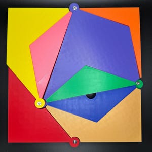 Peut inclure: Un puzzle g&eacute;om&eacute;trique color&eacute; avec diverses formes et couleurs, notamment rouge, jaune, orange, rose, vert, bleu et beige. Le puzzle est maintenu par de petites attaches rondes. Le design g&eacute;n&eacute;ral est un carr&eacute; avec un motif complexe et multicolore.