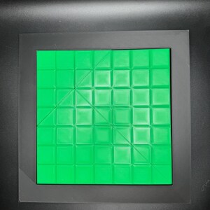 K&ouml;nnte beinhalten: Ein gr&uuml;nes quadratisches Puzzlebrett mit einem Gittermuster und diagonalen Linien. Das Brett ist aus Kunststoff und hat eine glatte Oberfl&auml;che.