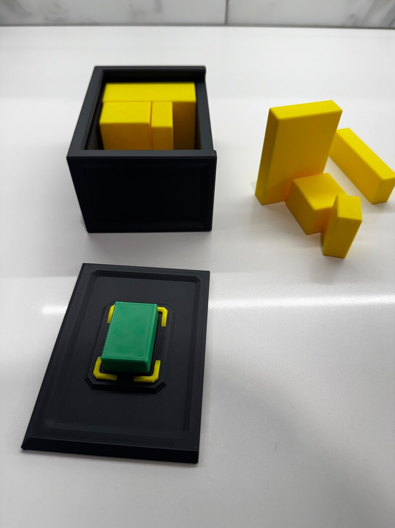 Pu&ograve; includere: Una scatola nera con un blocco verde all'interno. La scatola ha un bordo giallo. Ci sono blocchi gialli fuori dalla scatola.