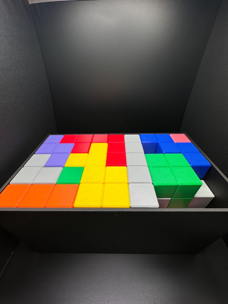Op de afbeelding: Een kleurrijke puzzel gemaakt van kleine vierkante blokken in een houten doos. De blokken zijn in een patroon gerangschikt met verschillende kleuren, waaronder rood, blauw, groen, geel, oranje en grijs.