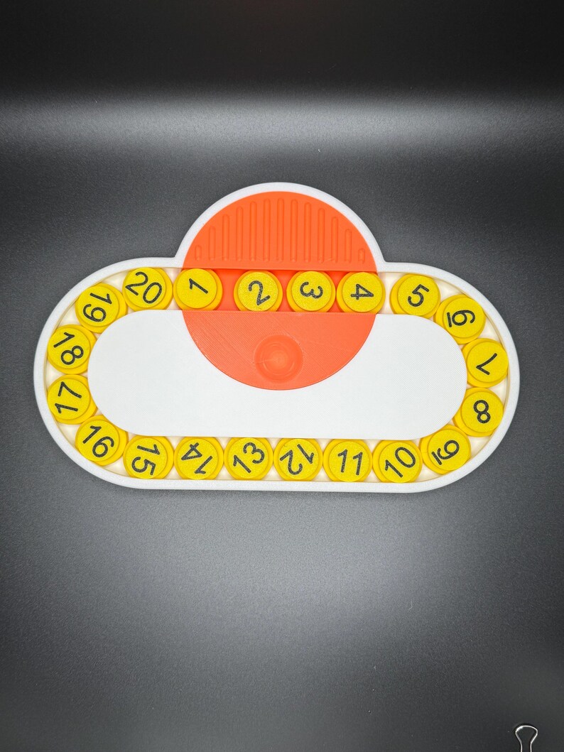 May include: A white and orange plastic toy with a circular track of yellow numbered pieces. The numbers 1 through 20 are visible on the track. The toy is designed to help children learn to count.