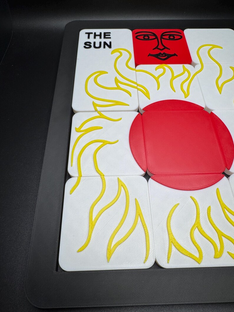 May include: A puzzle game featuring white tiles with yellow flame designs and a red sun. One tile reads "THE SUN". The game is set in a black frame.