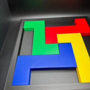 Op de afbeelding: Een kleurrijk puzzelspel met geometrische vormen in groen, rood, geel en blauw. De puzzelstukken zijn geplaatst in een zwart frame, wat een visueel aantrekkelijk ontwerp cre&euml;ert. De stukken zijn gemaakt van een stevig materiaal.