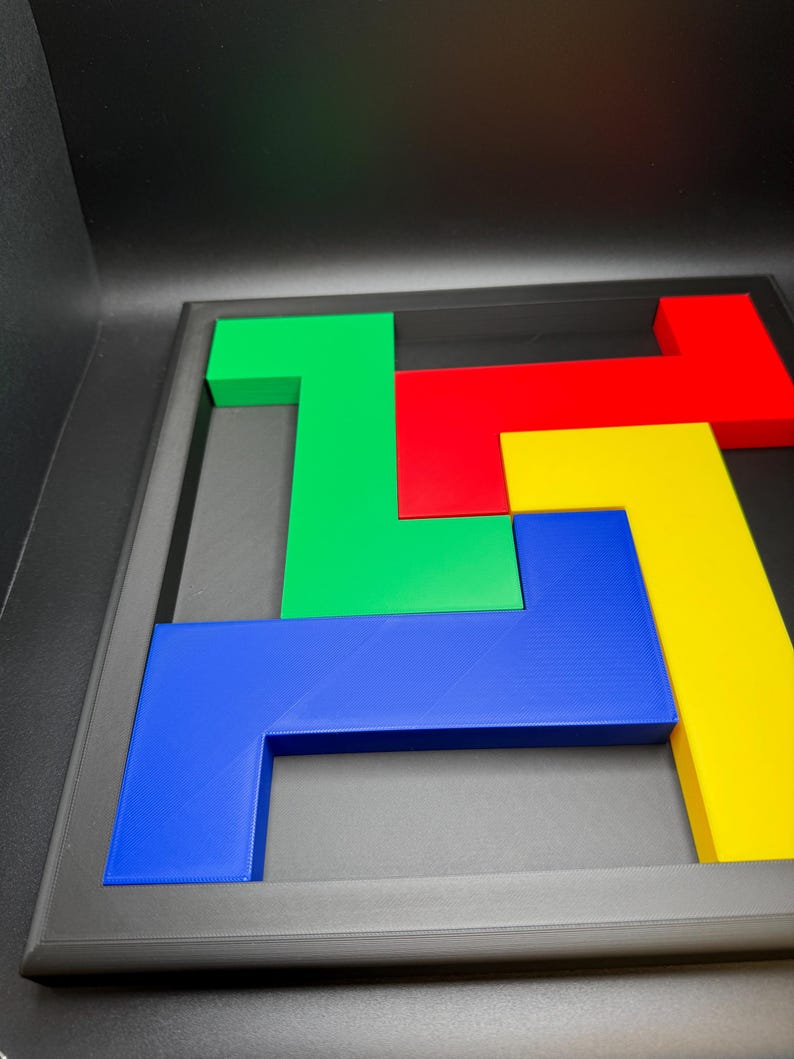 Op de afbeelding: Een kleurrijk puzzelspel met geometrische vormen in groen, rood, geel en blauw. De puzzelstukken zijn geplaatst in een zwart frame, wat een visueel aantrekkelijk ontwerp cre&euml;ert. De stukken zijn gemaakt van een stevig materiaal.