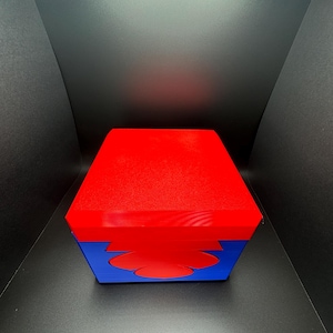 May include: A red and blue box with a unique design. The box has a red top and a blue bottom with a red cutout in the shape of a flower.