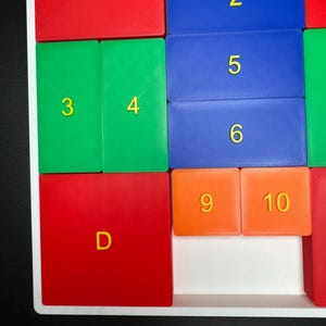 K&ouml;nnte beinhalten: Nahaufnahme eines bunten Puzzles mit roten, gr&uuml;nen, blauen und orangen Kacheln. Die Kacheln haben Buchstaben und Zahlen darauf, darunter A, 3, 4, 2, 5, 6, 9, 10 und D.