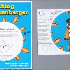 Puede incluir: Un juego de trucos de magia "Vanishing Hamburger" de McDonald's. La tarjeta azul presenta el texto "The Vanishing Hamburger" e ilustraciones de hamburguesas. El juego incluye instrucciones y un disco giratorio con un personaje de Hamburglar.