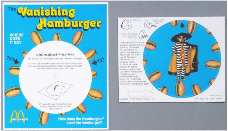 Puede incluir: Un juego de trucos de magia "Vanishing Hamburger" de McDonald's. La tarjeta azul presenta el texto "The Vanishing Hamburger" e ilustraciones de hamburguesas. El juego incluye instrucciones y un disco giratorio con un personaje de Hamburglar.