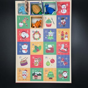 May include: Christmas advent calendar with 24 compartments, each holding a small toy or decoration. The calendar has a festive design with colourful squares, including a snowman, Santa, and Christmas tree.
