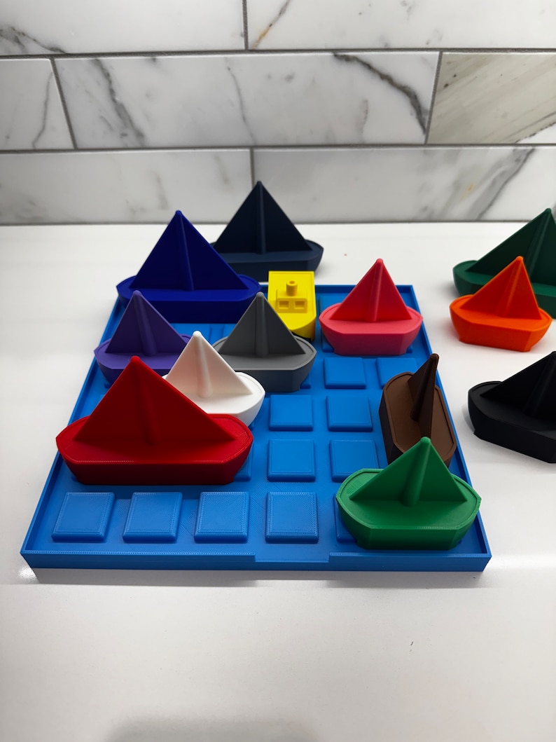 May include: A blue tray with a grid pattern holds a variety of colorful toy boats. The boats are made of plastic and are shaped like sailboats. The boats are arranged in a random pattern on the tray.