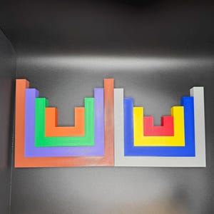 May include: Two colorful wooden block puzzles. One puzzle features orange, green, purple, and brown blocks. The other puzzle has red, yellow, blue, and gray blocks. The blocks are arranged in a square shape.