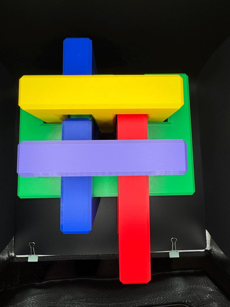 May include: A colorful wooden puzzle with four pieces. The pieces are red, yellow, blue, and purple. The puzzle is in the shape of a cross.