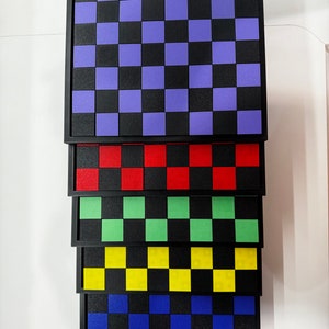 May include: A stack of six black framed checkerboards with different colored squares. The top checkerboard has purple squares, the next has red squares, the next has green squares, the next has yellow squares, the next has blue squares, and the bottom checkerboard has orange squares.