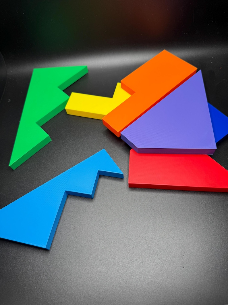 May include: A set of six colorful puzzle pieces made of wood. The pieces are shaped like different geometric shapes, including triangles, squares, and rectangles. The pieces are arranged in a random order on a black surface.