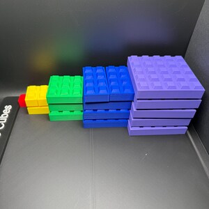 May include: A collection of colorful building blocks in various sizes and colors, including red, yellow, green, blue, and purple. The blocks are arranged in a stepped pattern, showcasing their different dimensions and shapes. The blocks have a textured surface.