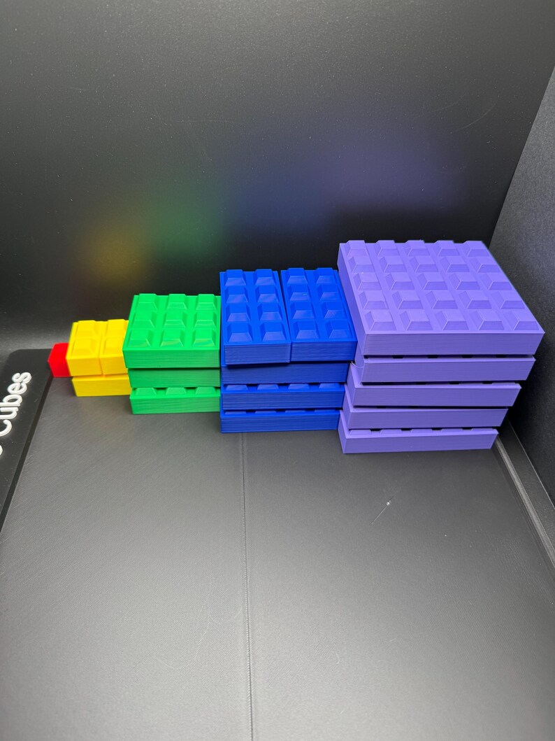 May include: A collection of colorful building blocks in various sizes and colors, including red, yellow, green, blue, and purple. The blocks are arranged in a stepped pattern, showcasing their different dimensions and shapes. The blocks have a textured surface.
