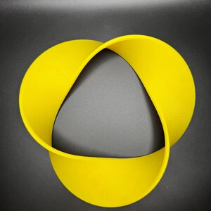 May include: A yellow, three-dimensional, Mobius strip-shaped object. The object is made of a flexible material and is shaped like a continuous loop.