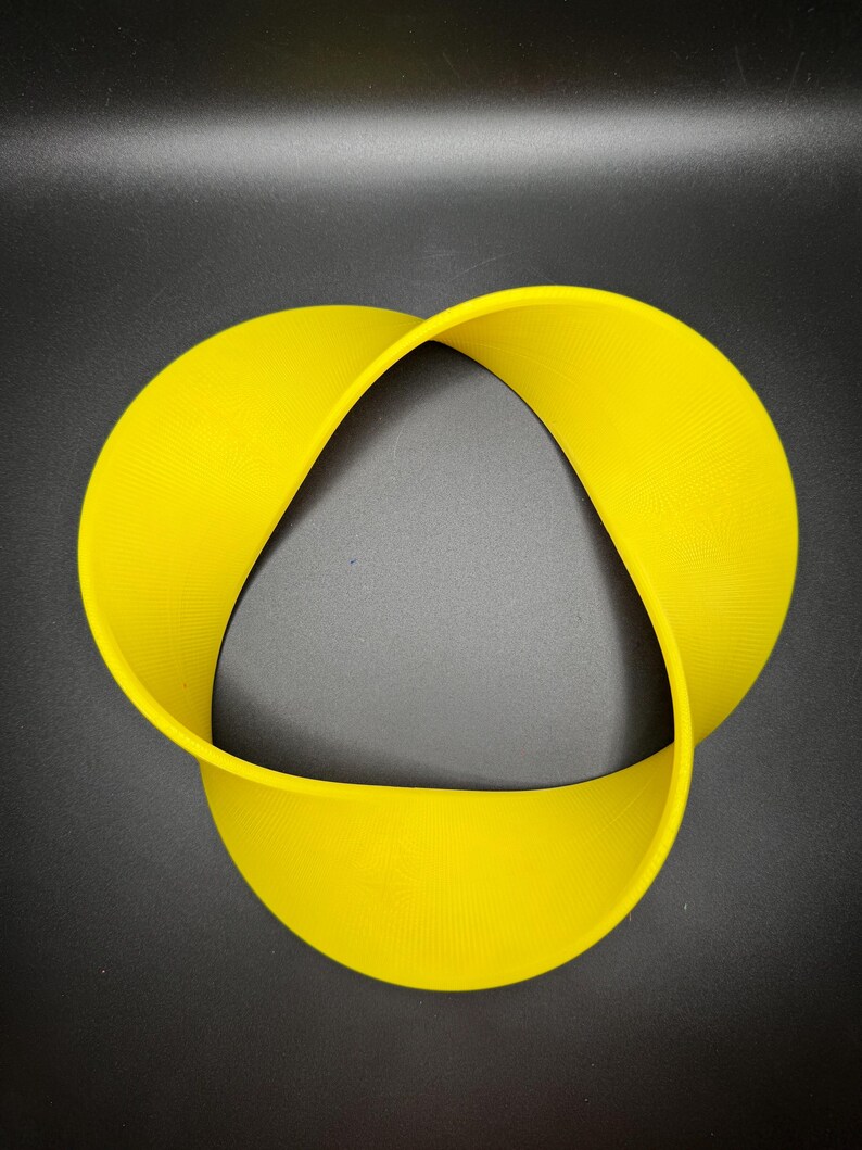 May include: A yellow, three-dimensional, Mobius strip-shaped object. The object is made of a flexible material and is shaped like a continuous loop.
