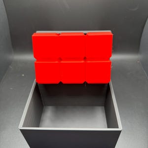 May include: A small, black box with a red lid. The lid is made of multiple squares.