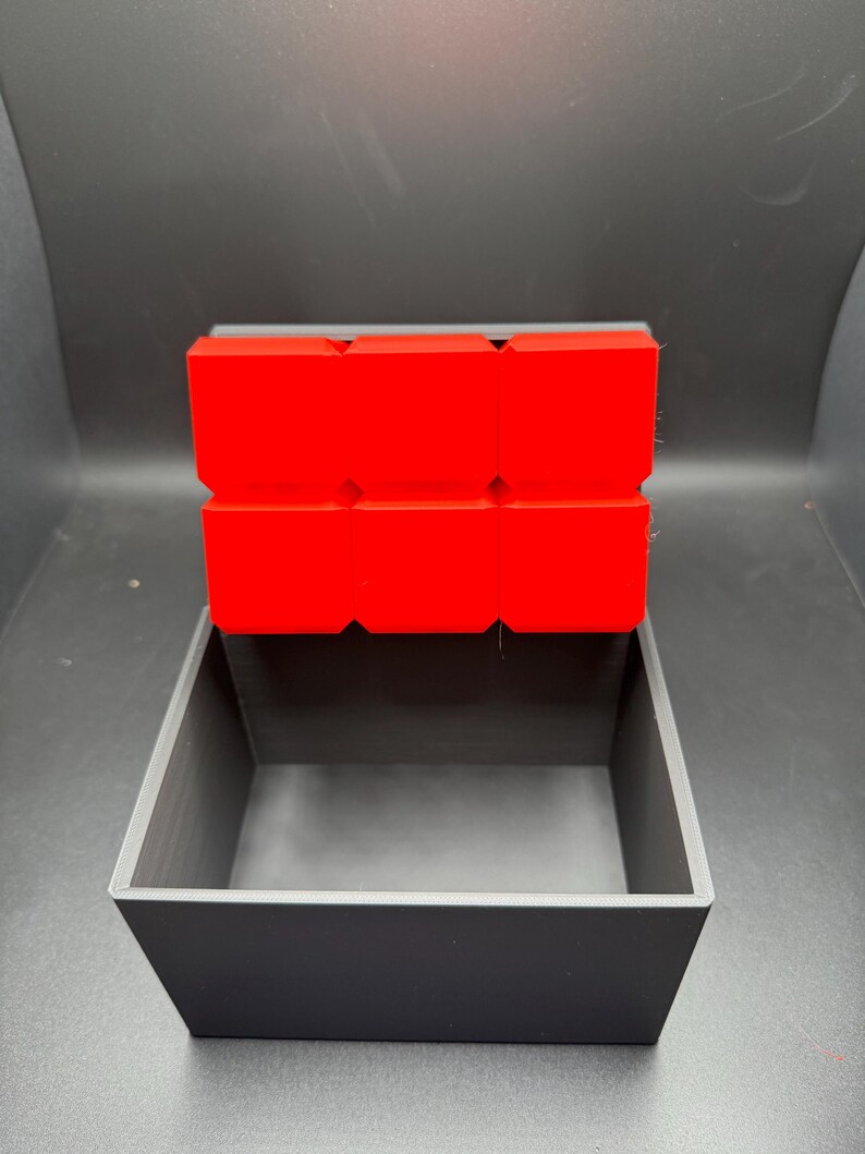 May include: A small, black box with a red lid. The lid is made of multiple squares.