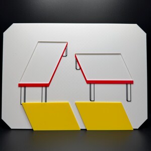 May include: Geometric art piece featuring a white rectangular base with cut-out shapes. Two red-lined trapezoids sit atop black supports. Below, two yellow diamond shapes are positioned. The artwork is set against a black background.