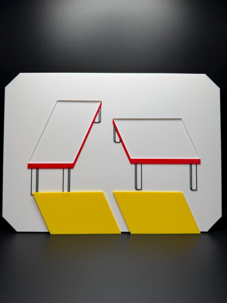 May include: Geometric art piece featuring a white rectangular base with cut-out shapes. Two red-lined trapezoids sit atop black supports. Below, two yellow diamond shapes are positioned. The artwork is set against a black background.